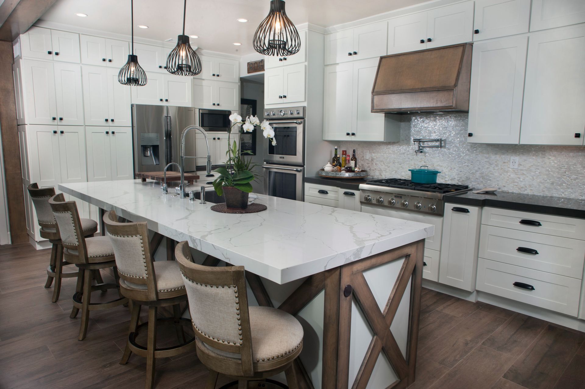 Modern white kitchen with a large island, stainless steel appliances, and dark wood accents.