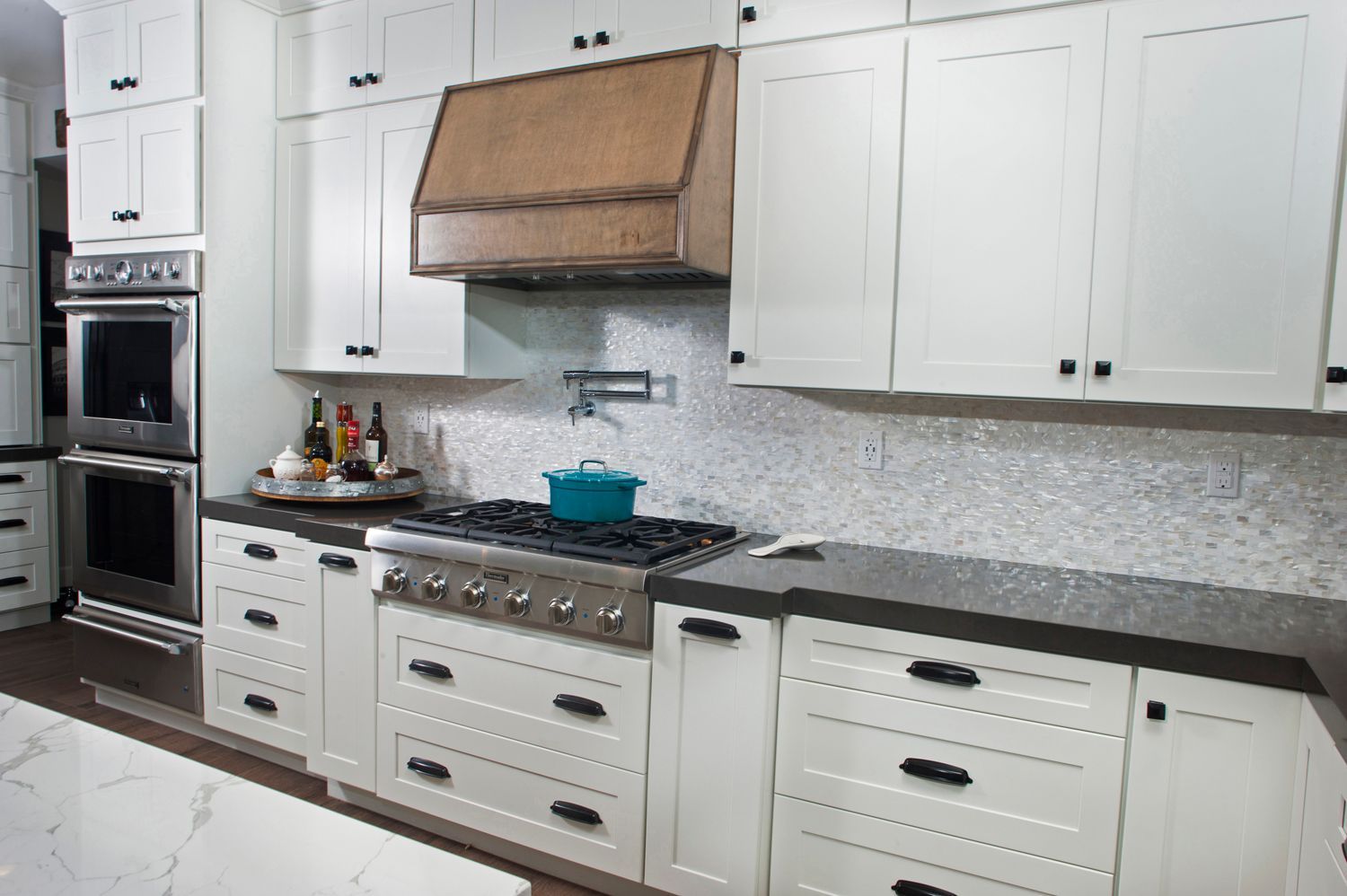 White kitchen with stainless steel appliances, dark countertops, and a wood range hood.