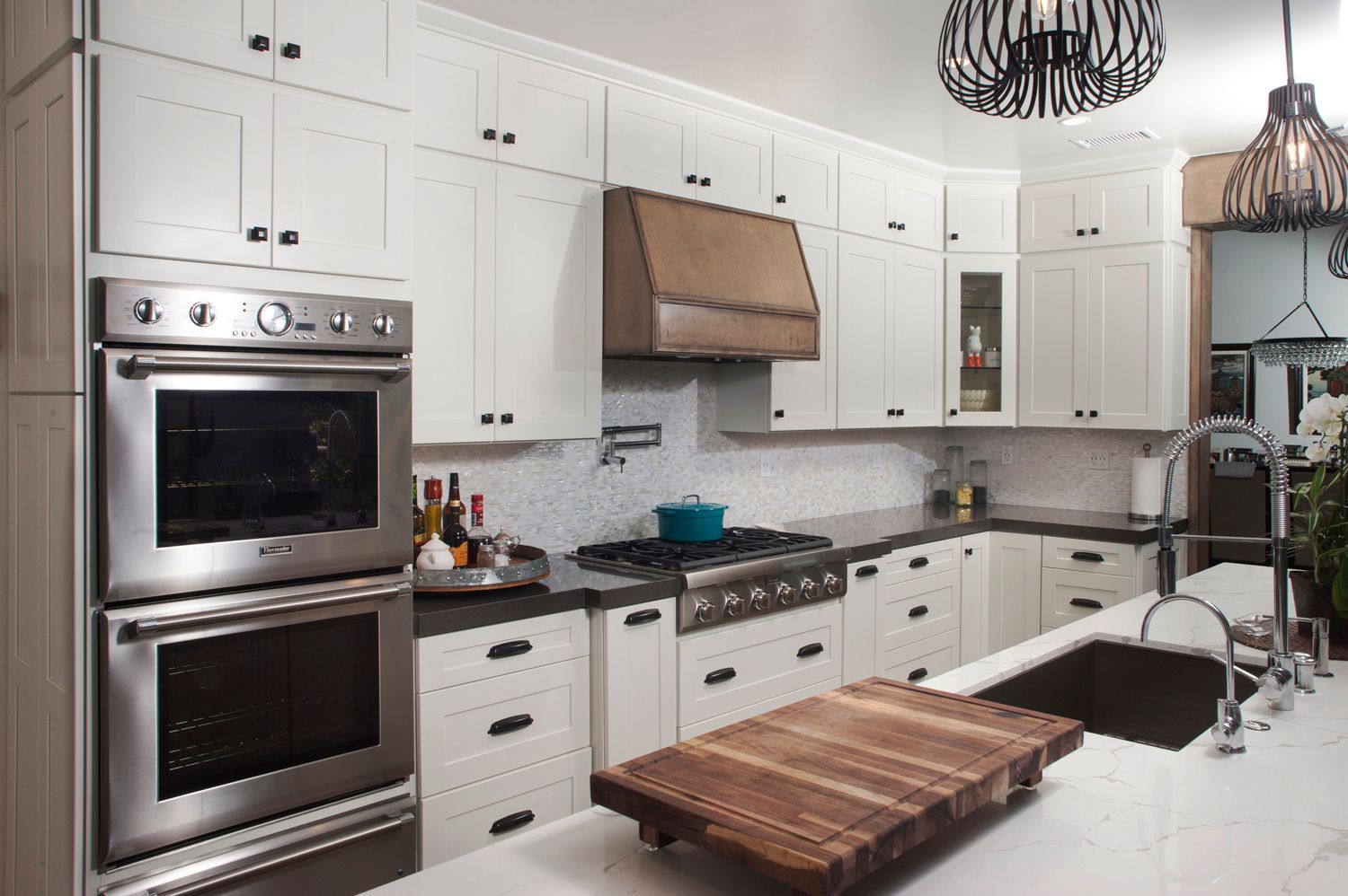 White kitchen with stainless steel appliances, dark countertops, and wooden accents.