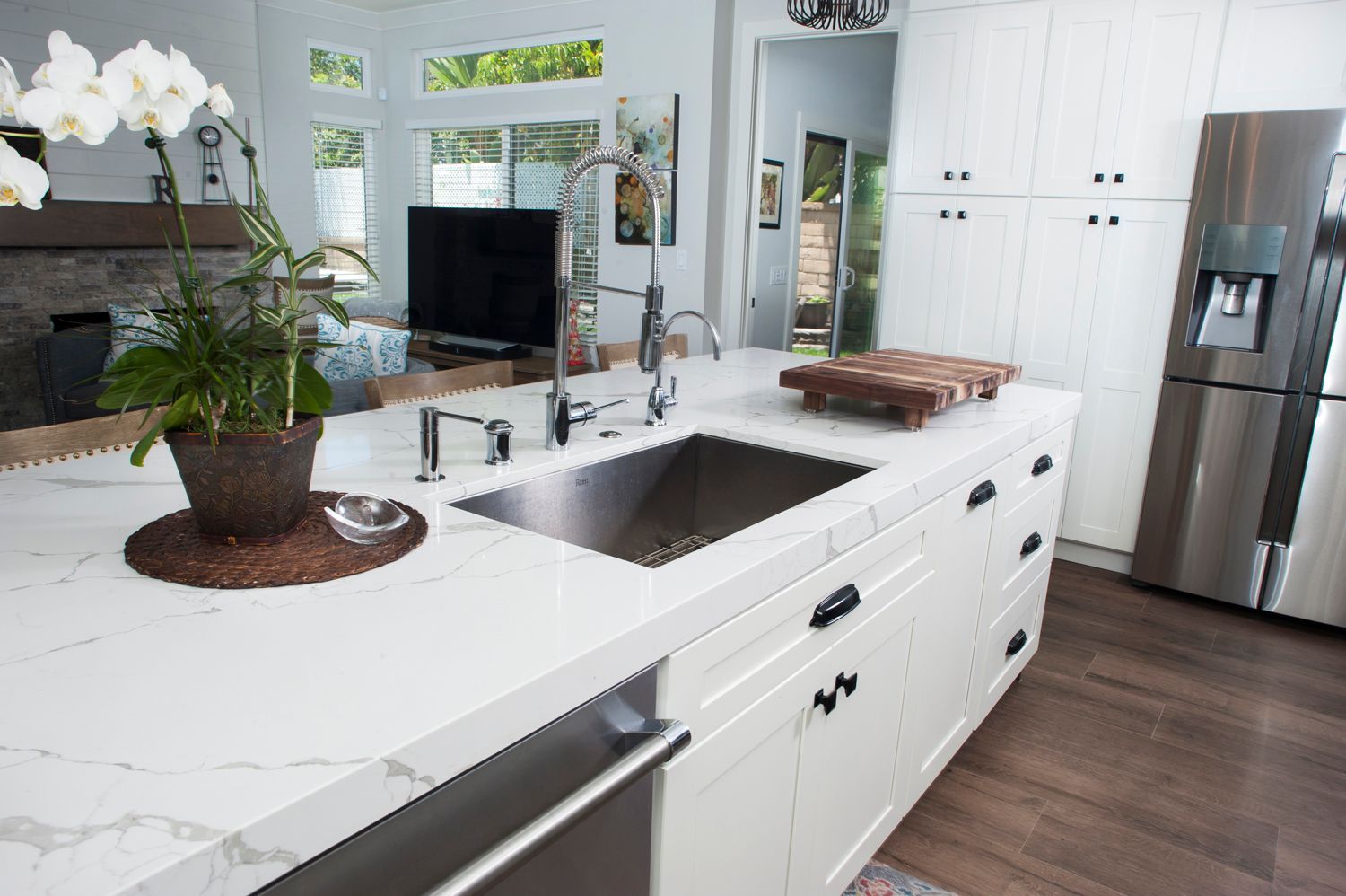 Modern kitchen with white countertops, stainless steel sink, and refrigerator.