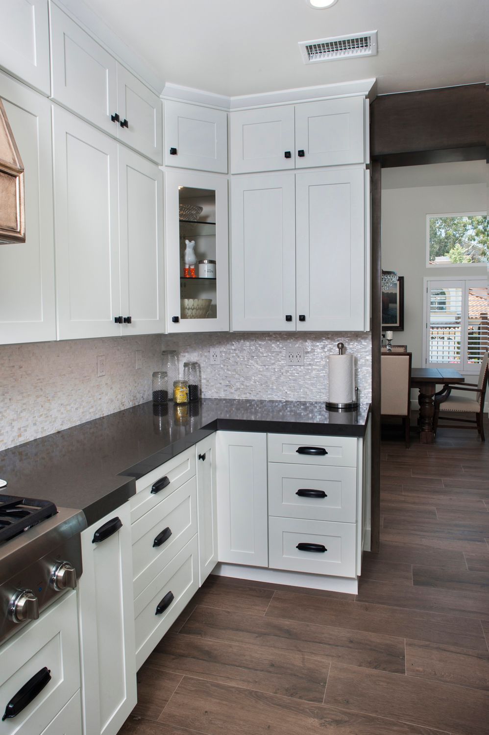 White kitchen with dark countertops, black hardware, and mosaic backsplash.