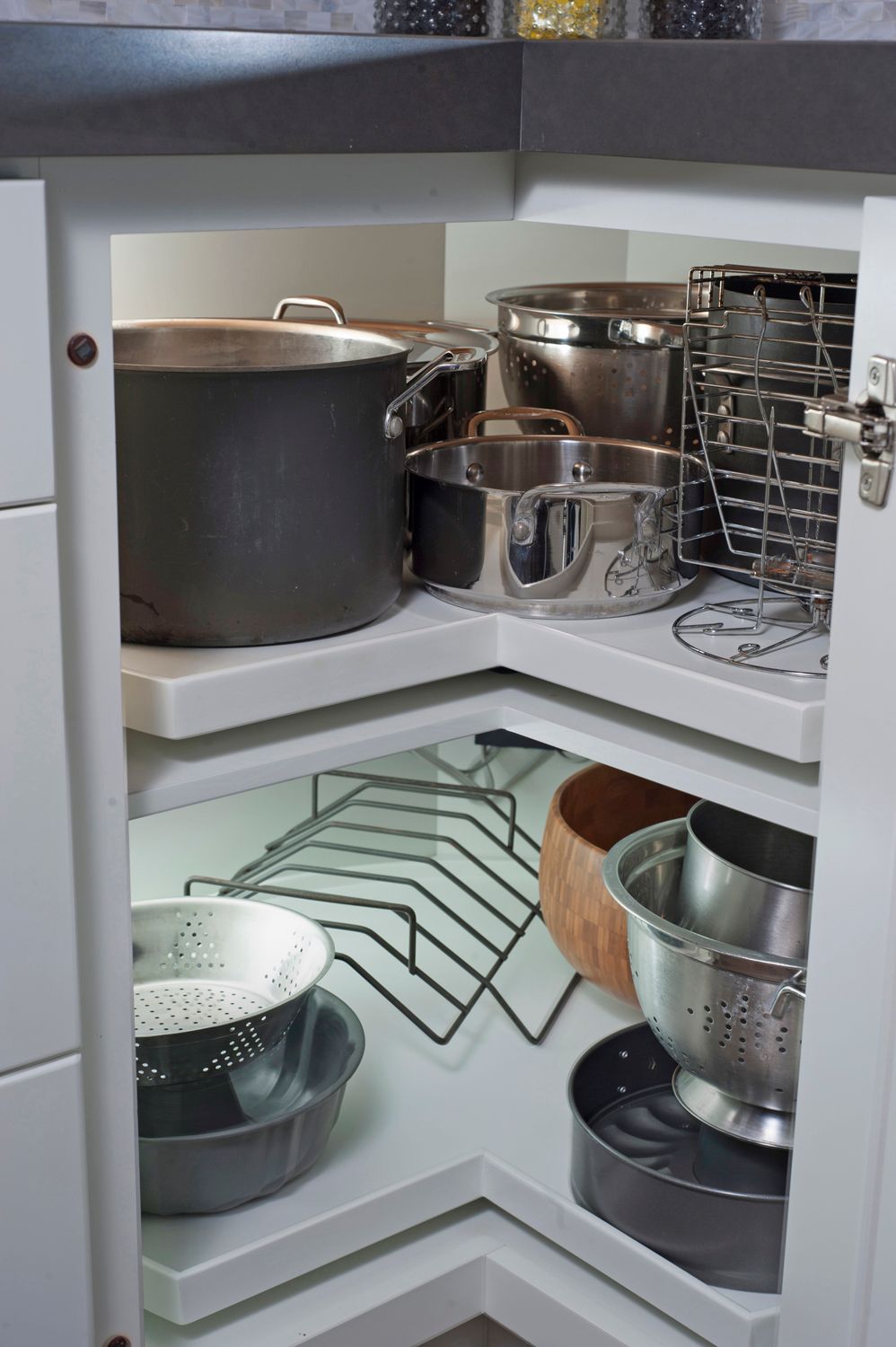 A kitchen cabinet with pull-out shelves holding pots, pans, and colanders, organized for easy access.