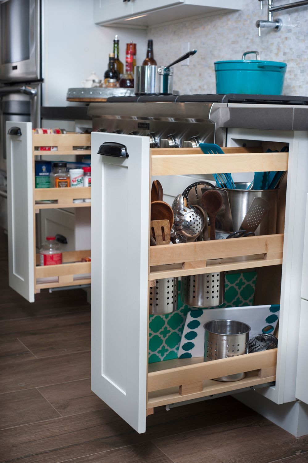 White pull-out kitchen cabinets with spices and cooking utensils. Wooden shelves, white cabinets, turquoise accent.
