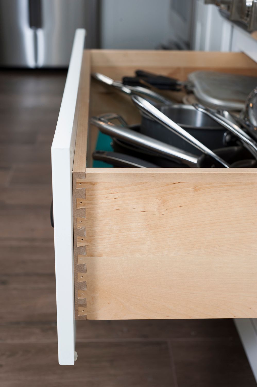 Open kitchen drawer, dovetail joints visible. Inside, utensils and small cookware.