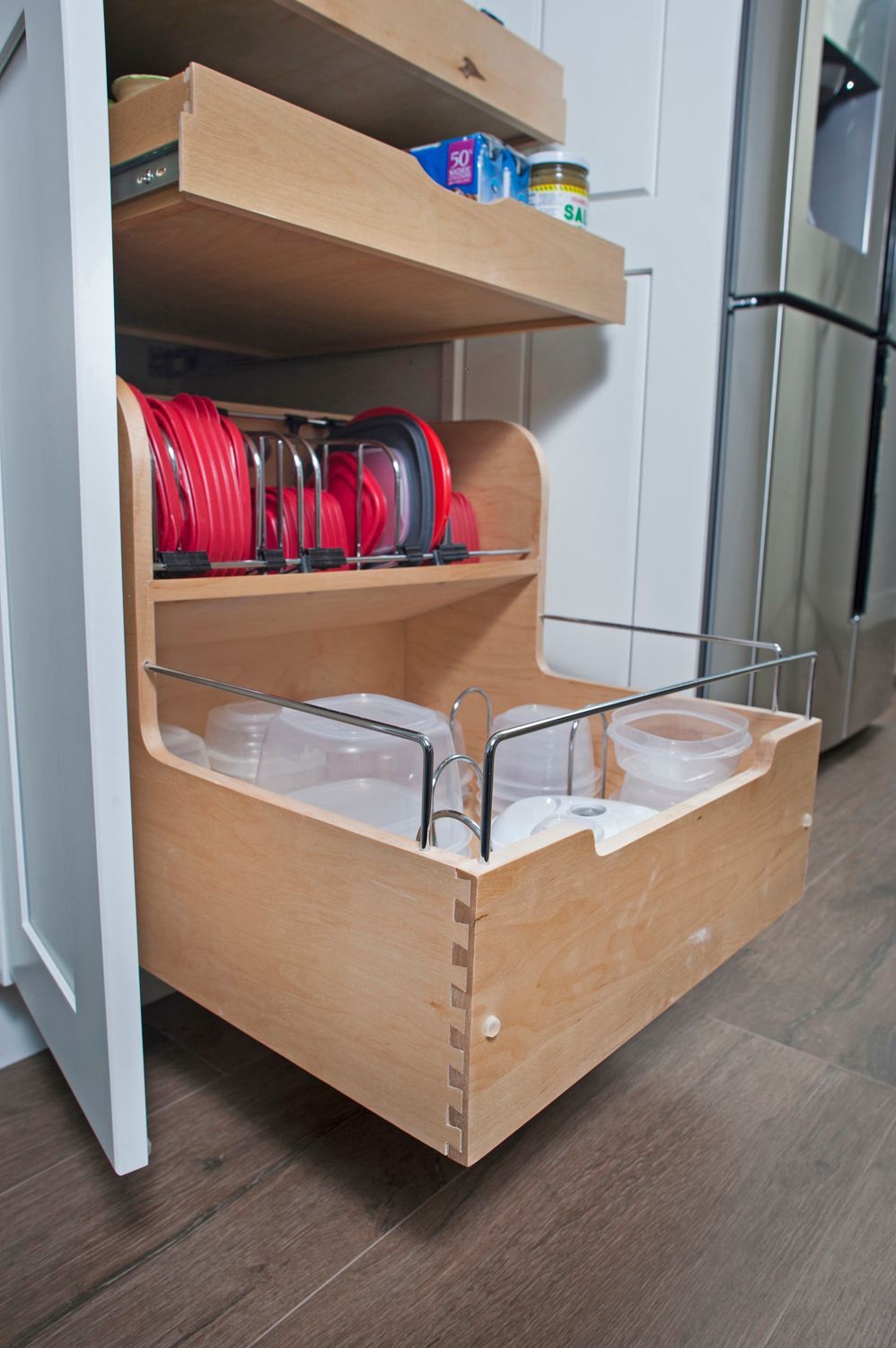 Pull-out kitchen cabinet with storage for lids and containers.  Wooden construction, white cabinet, and hardwood floor.