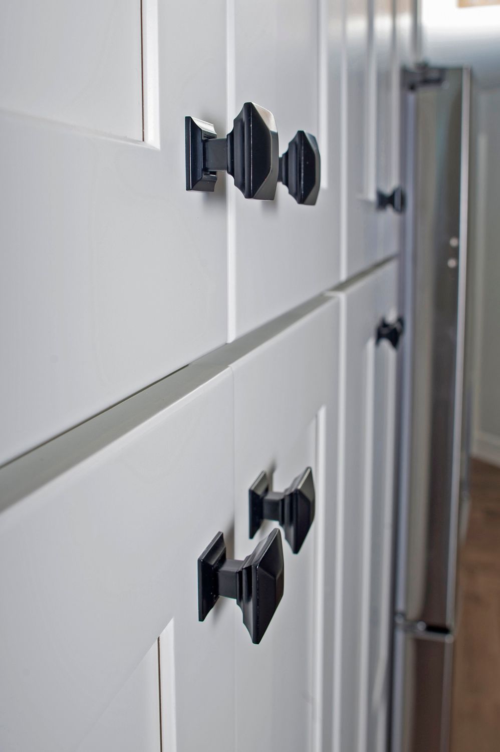 White kitchen cabinets with black geometric knobs.