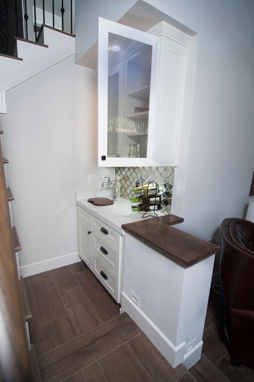 White built-in bar under stairs. White cabinets, marble countertop, wood bar top.