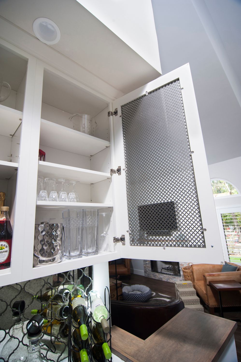 White kitchen cabinet open, revealing glassware and a patterned door panel.