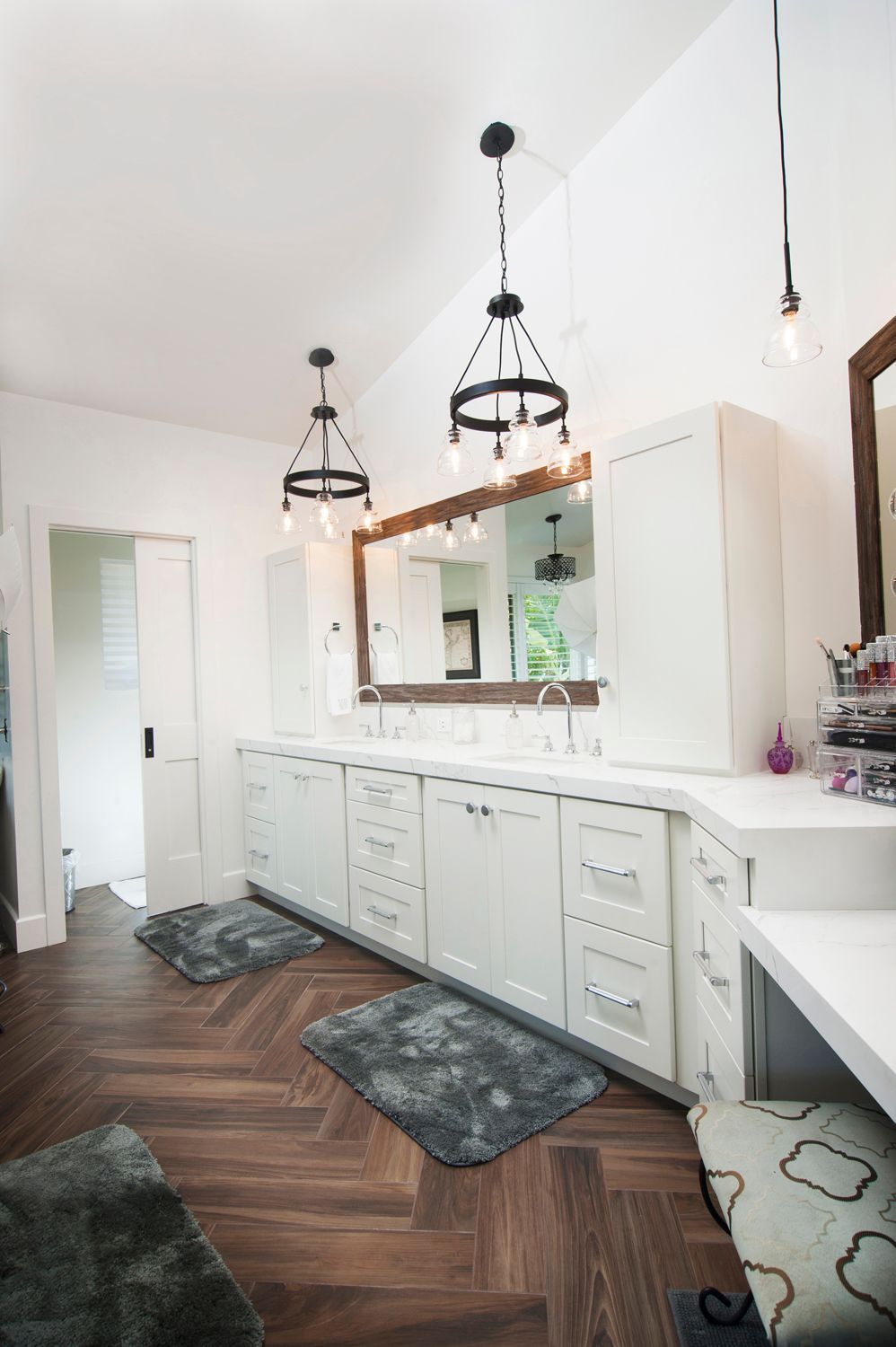 Spacious bathroom with white cabinets, dark wood floor, two chandeliers, and large mirror.