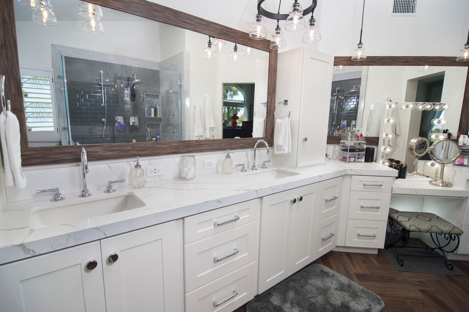 Spacious white bathroom with double sinks, large mirrors, and a makeup vanity; brown wood trim.