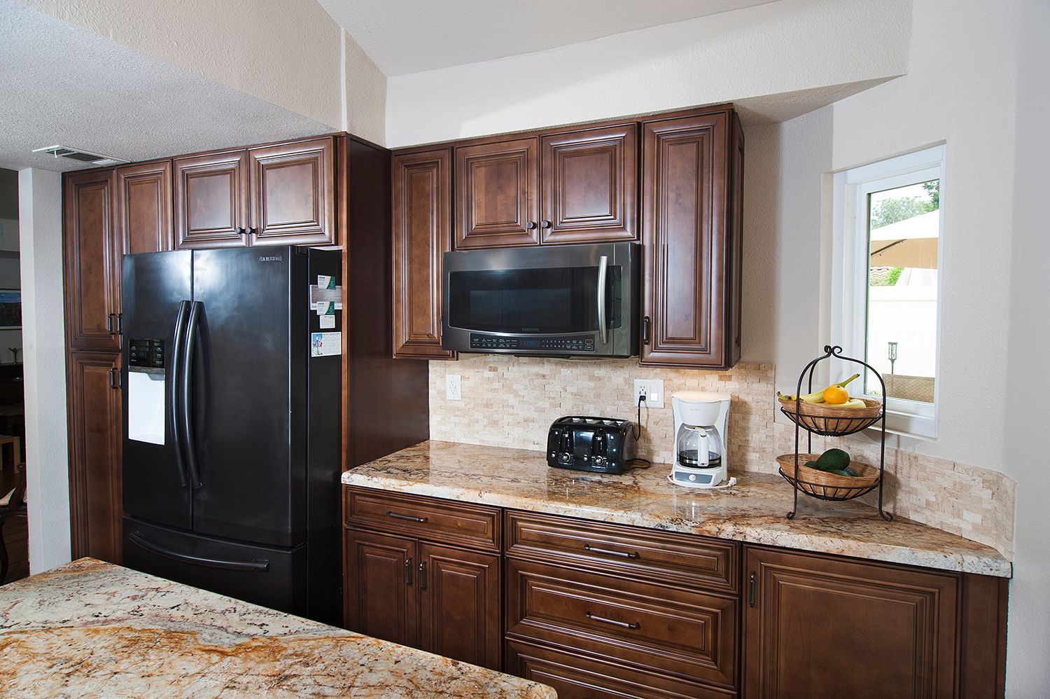 Kitchen with brown cabinets, granite countertops, black appliances. Window with view.