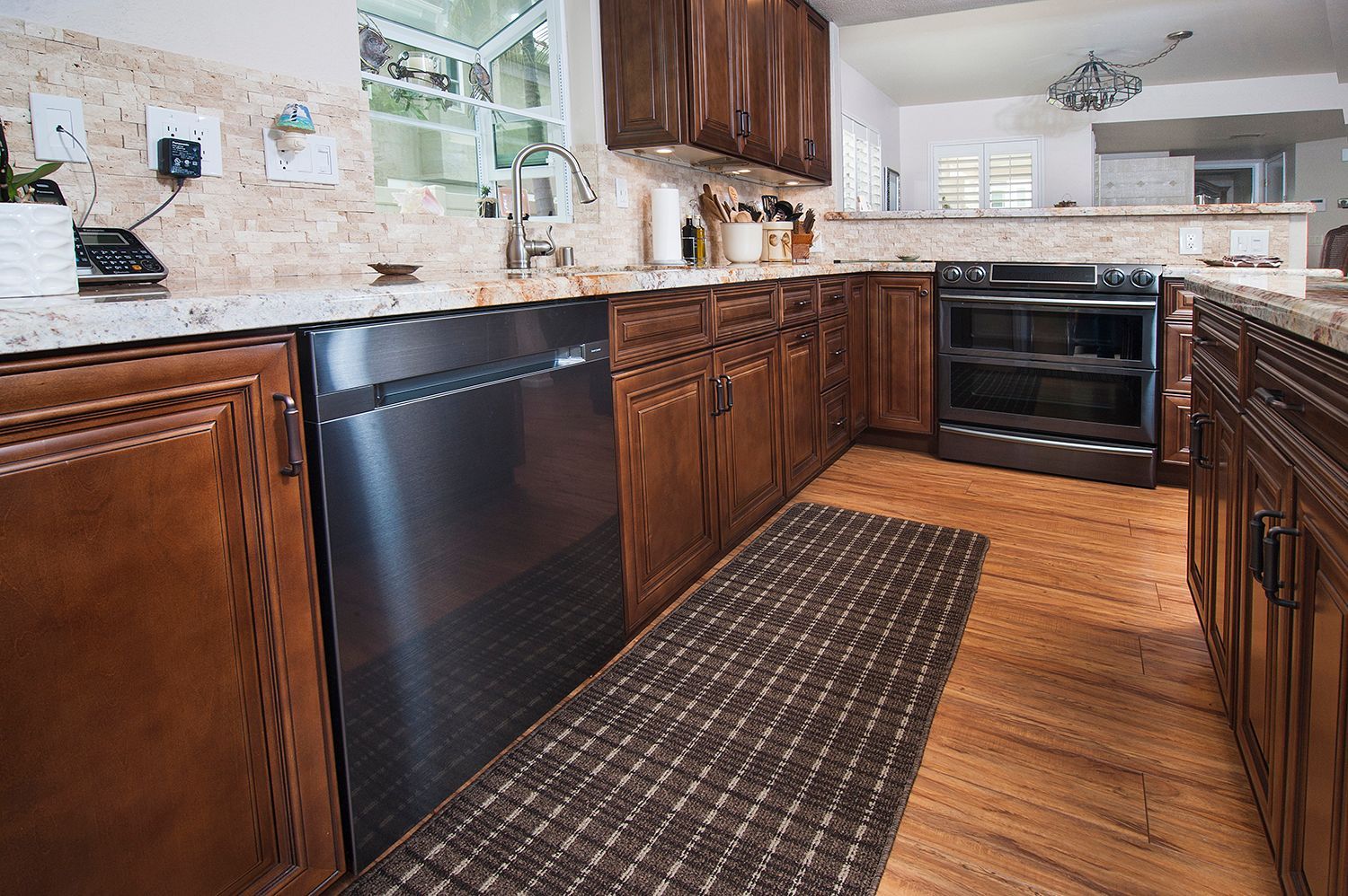 Kitchen with wooden cabinets, stainless steel appliances, granite countertops, and a checkered rug.