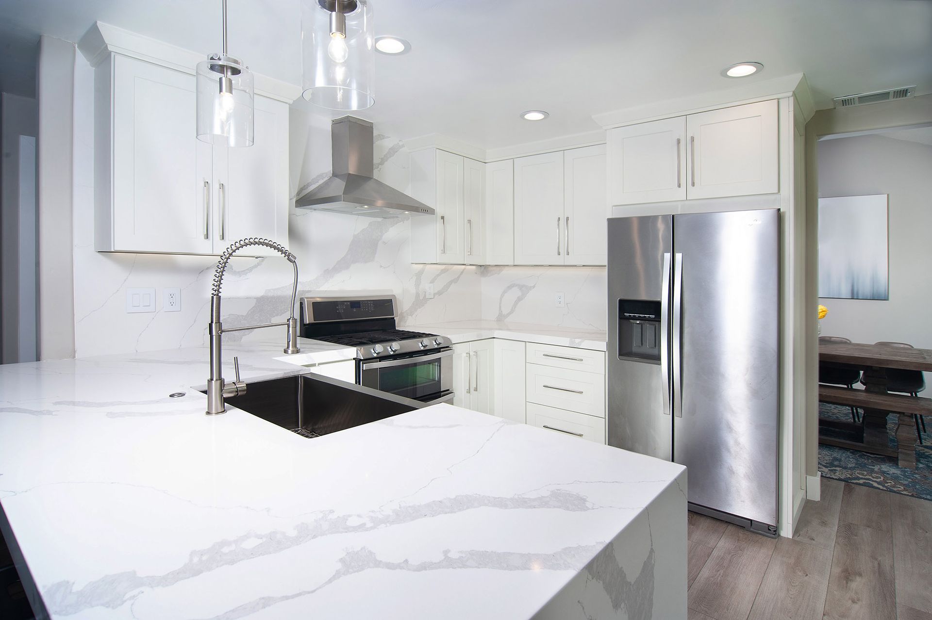 White kitchen with stainless steel appliances, island with a sink, and overhead lighting.