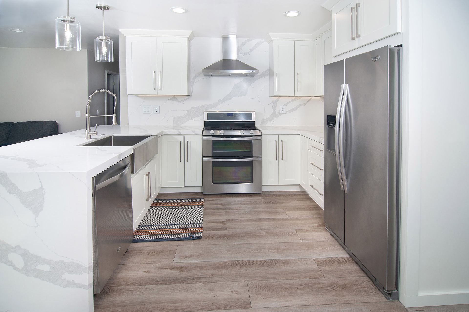 Modern white kitchen with stainless steel appliances, light wood floors, and marble backsplash.