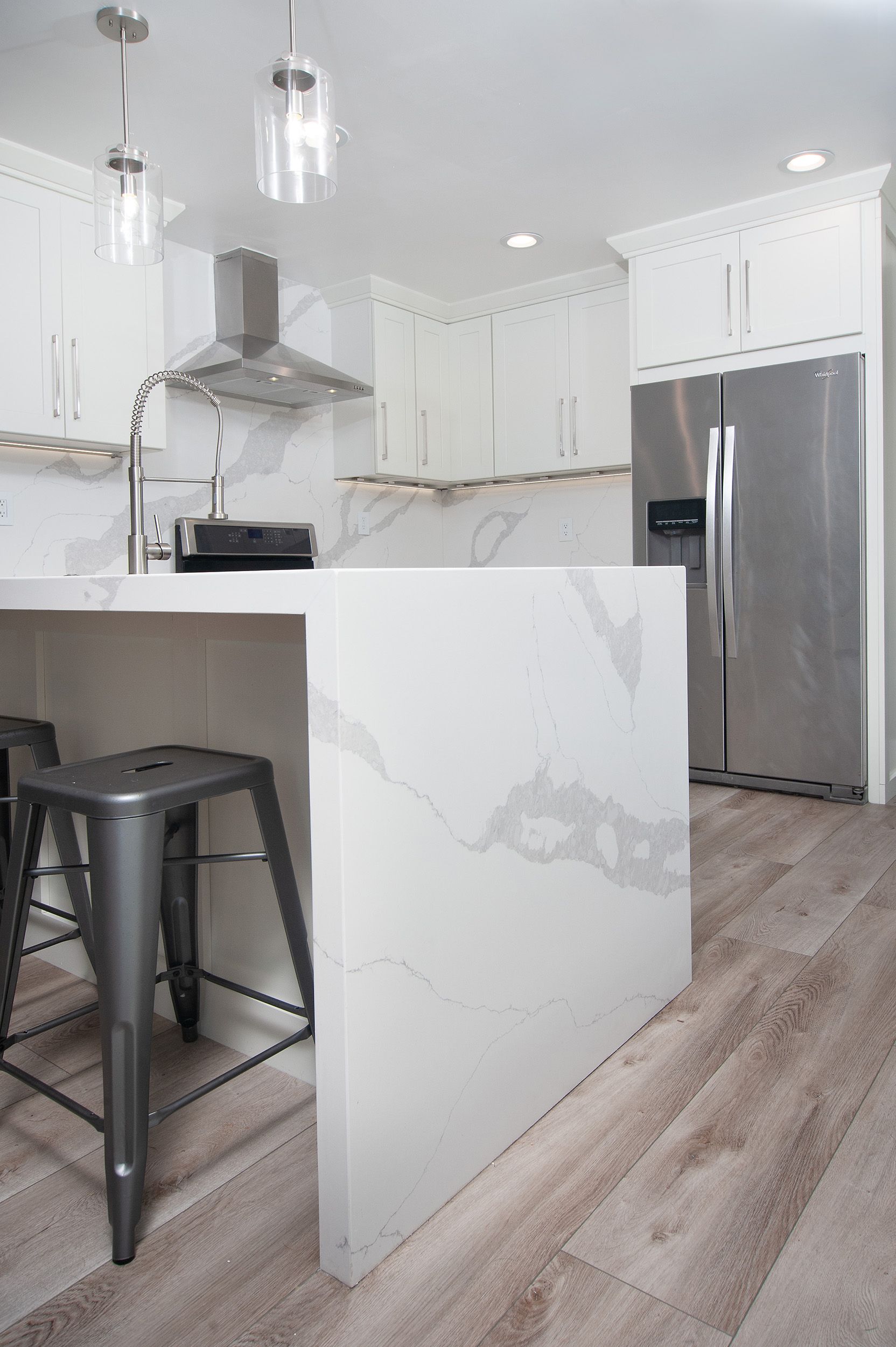 White kitchen with marble island, stainless steel appliances, and gray bar stools.