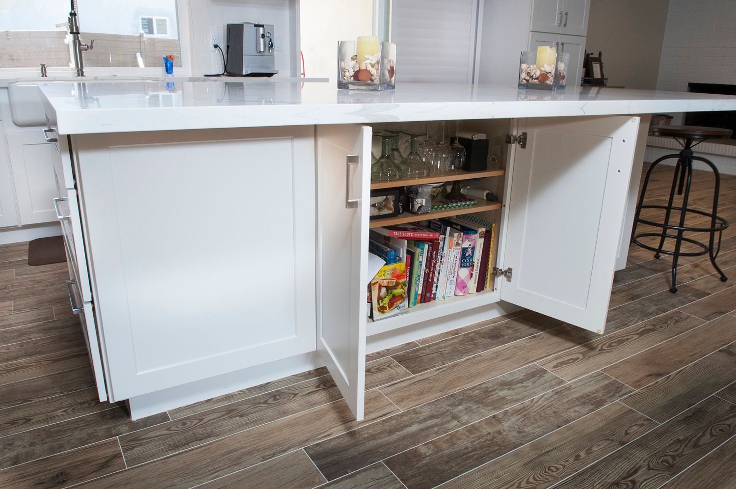 White kitchen island with open cabinets, showing shelves of glasses and magazines.