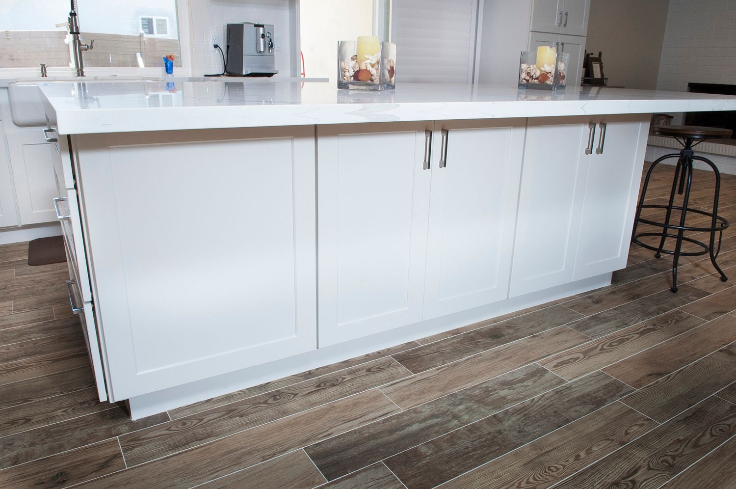 White kitchen island with cabinets, light countertop, and wood-look floor.