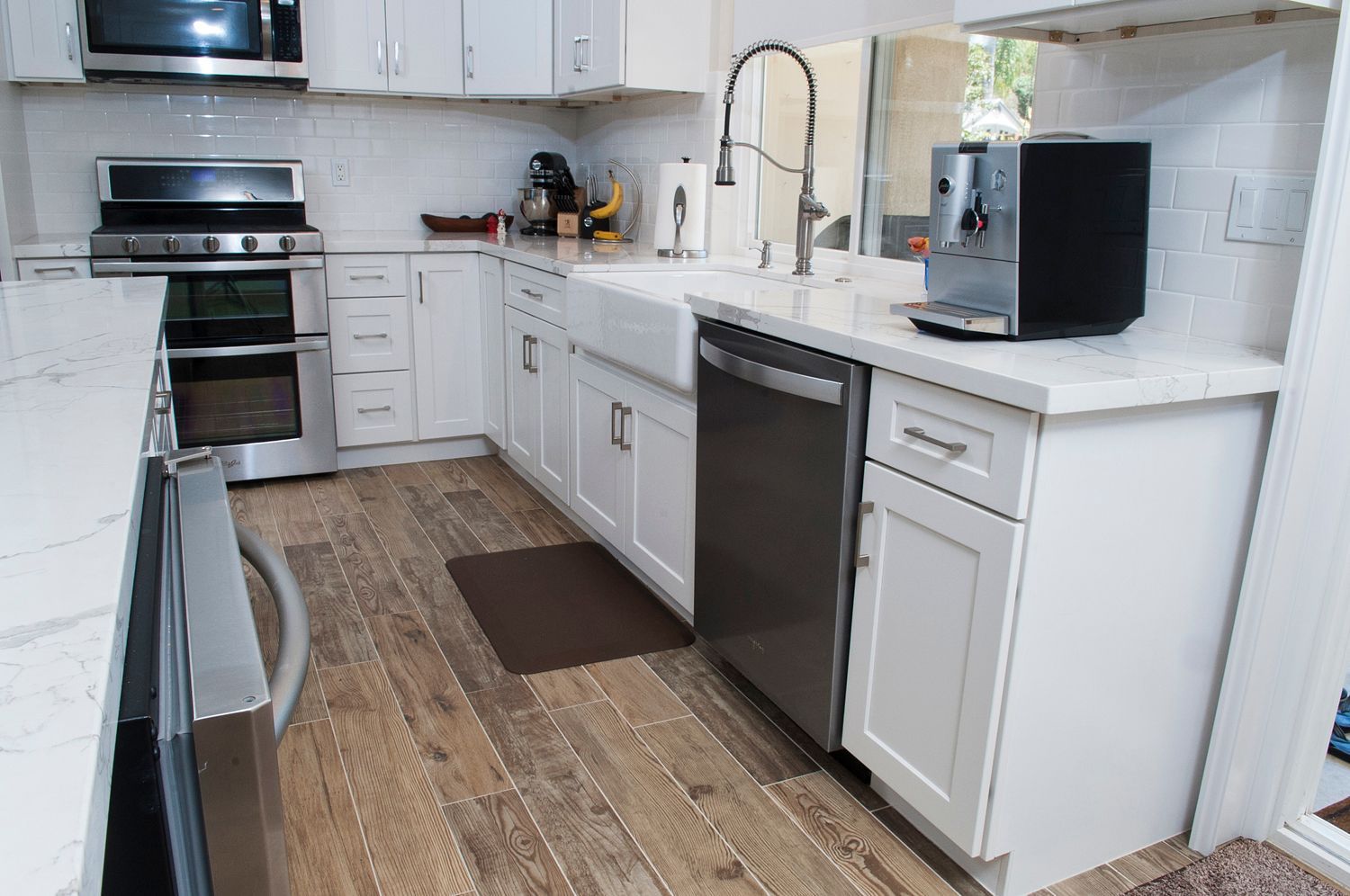 Modern white kitchen with stainless steel appliances, light wood floors, and a coffee machine on the counter.