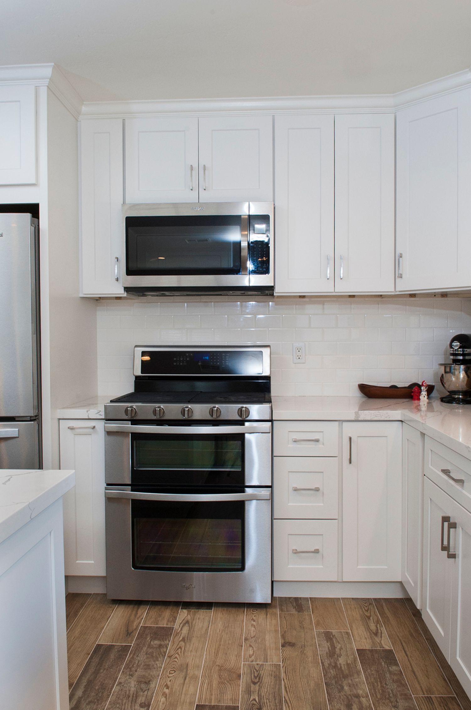 White kitchen with stainless steel appliances, including a double oven and microwave, against a white subway tile backsplash.