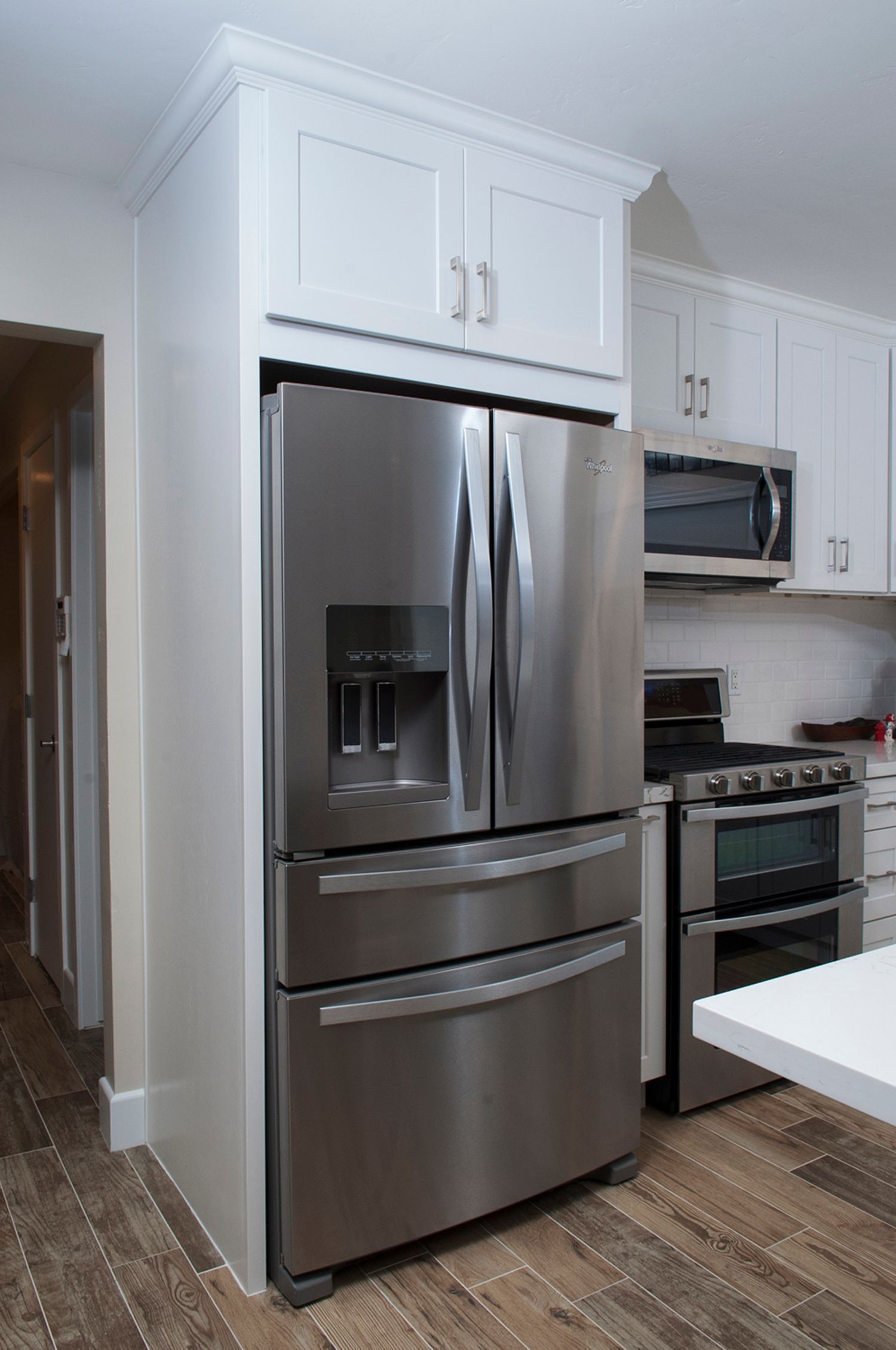 Stainless steel refrigerator in a white kitchen, with upper cabinets and a microwave visible.