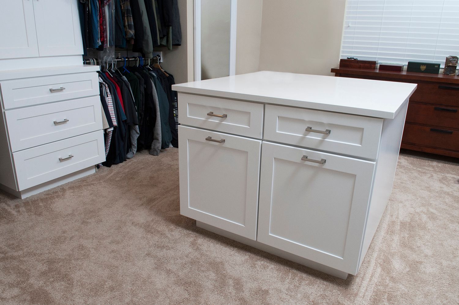 White closet island with drawers and cabinets in a bedroom with beige carpet.
