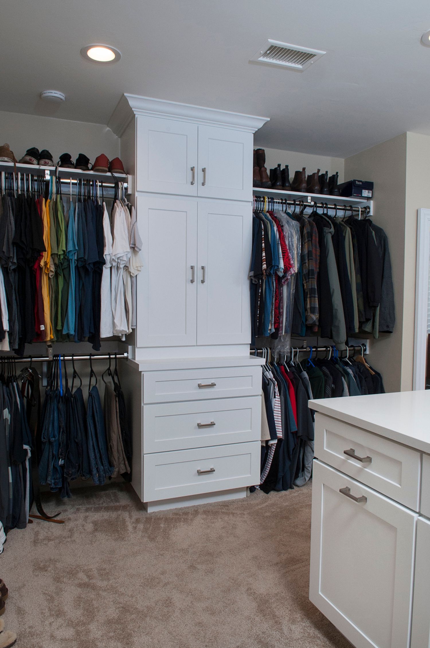 Walk-in closet with white cabinets, drawers, and hanging clothes. Beige carpet, and shoe shelves.