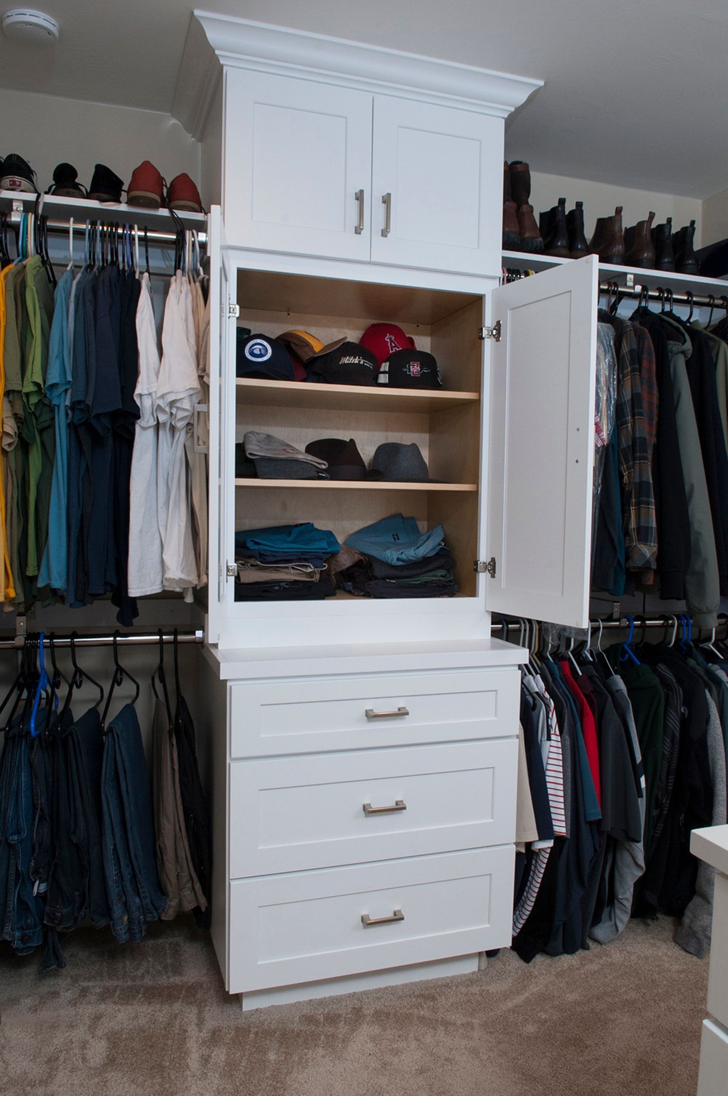 White closet storage unit with drawers, shelves, and cabinet, full of clothes and hats.