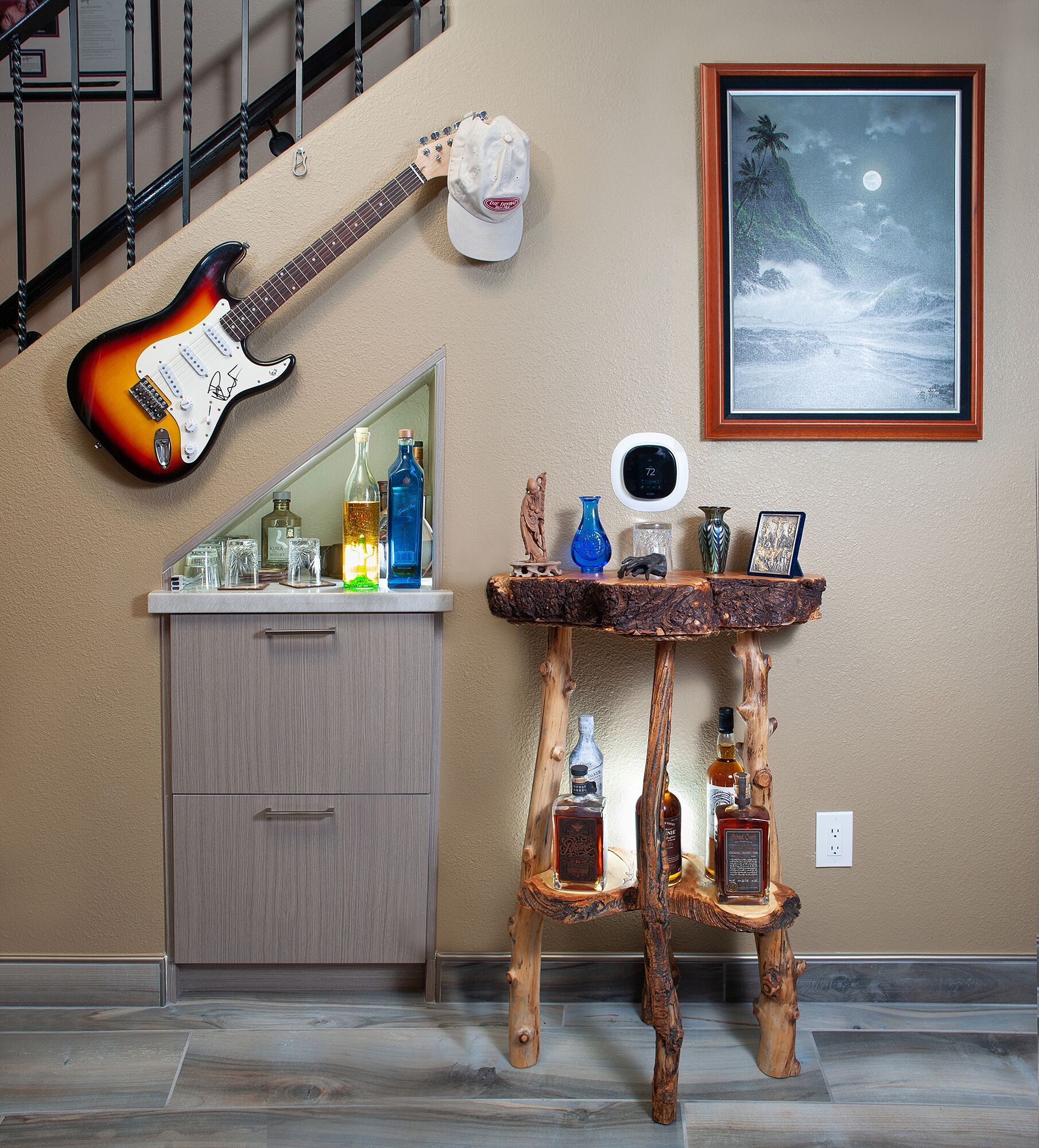 An indoor shot of a wall with a guitar, cabinet, and rustic table.  A framed print hangs nearby.