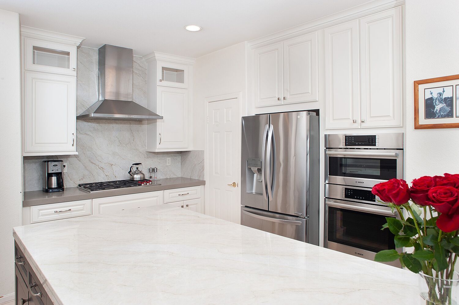 White kitchen with stainless steel appliances, marble countertops, and a bouquet of red roses.