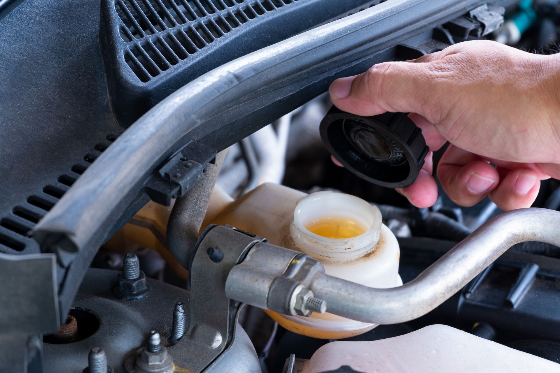 Hand opening a car's brake fluid reservoir. Beige fluid visible in a white container