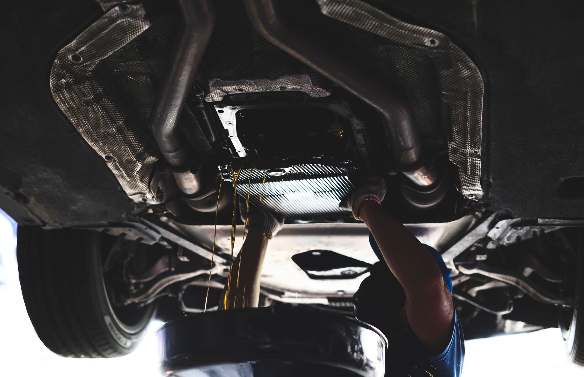 Mechanic draining oil from a car engine, seen from below