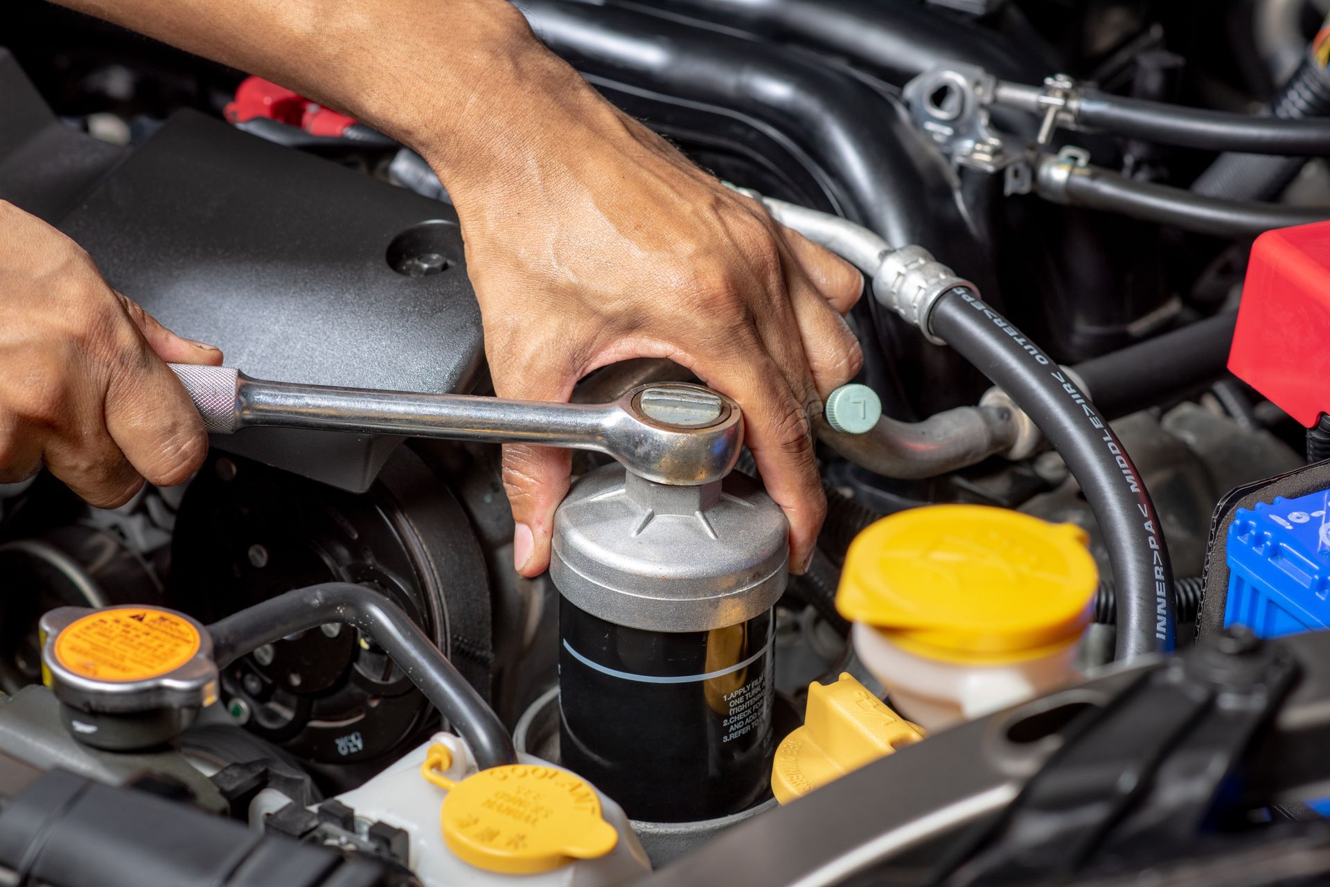 Person using a wrench to remove an oil filter from a car engine