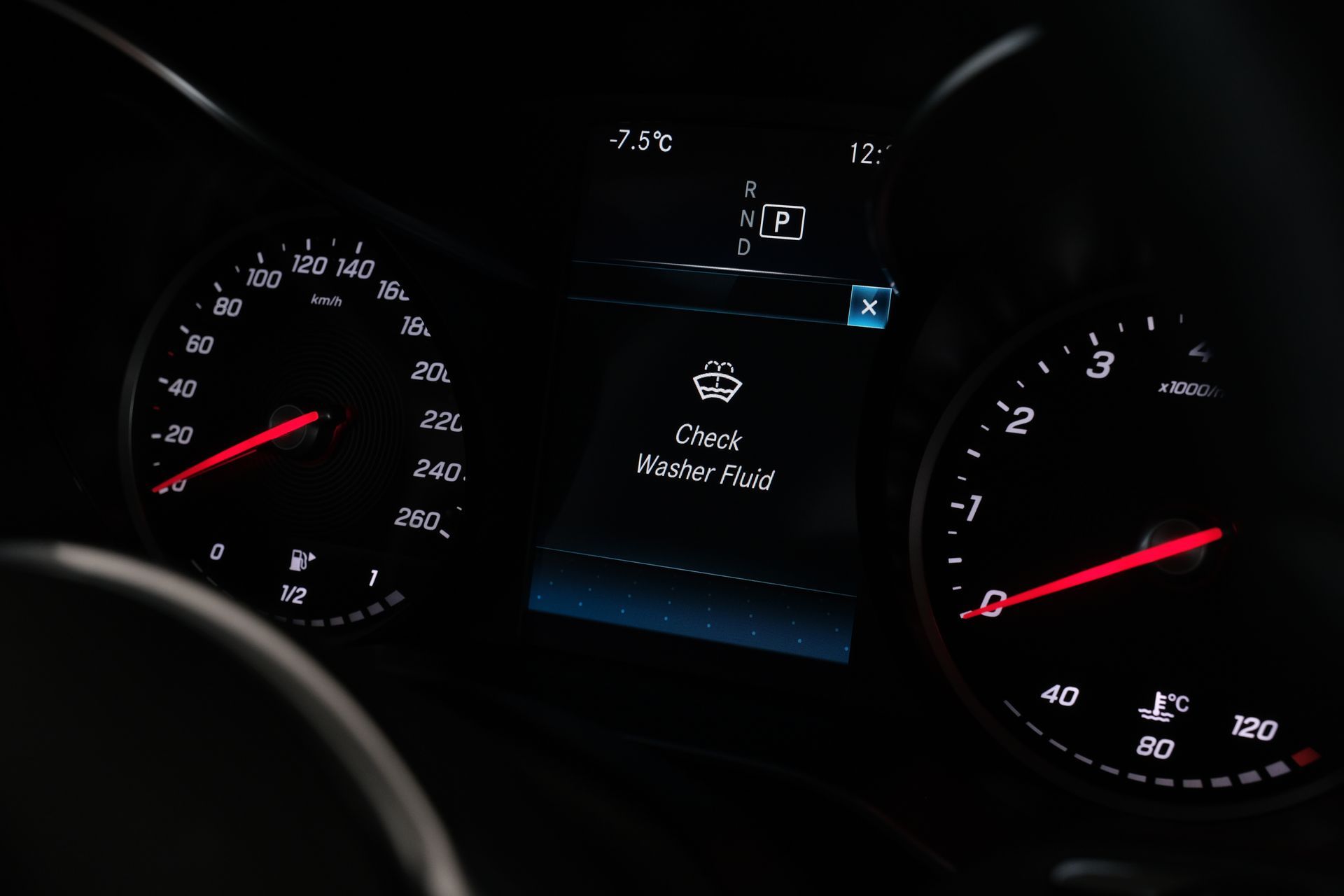 Car dashboard with illuminated gauges and a warning message to check window fluid