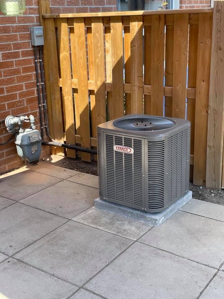 An air conditioner is sitting on a patio next to a wooden fence.