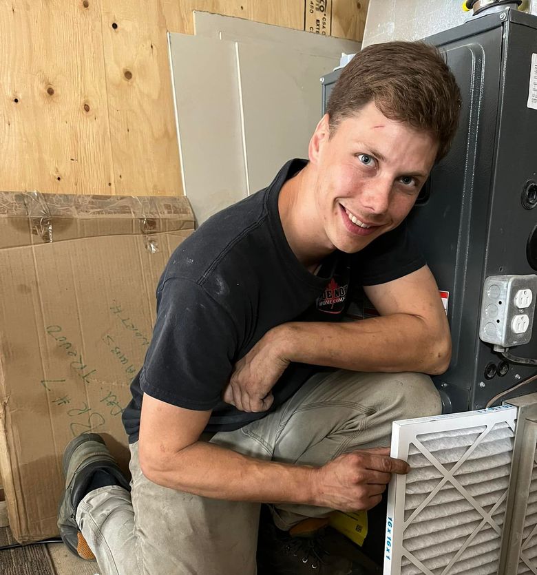 A man is kneeling down next to a machine and smiling.