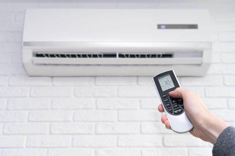 A person is holding a remote control in front of an air conditioner.