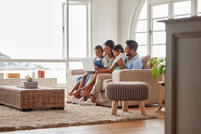 A family is sitting on a couch in a living room looking at a laptop.