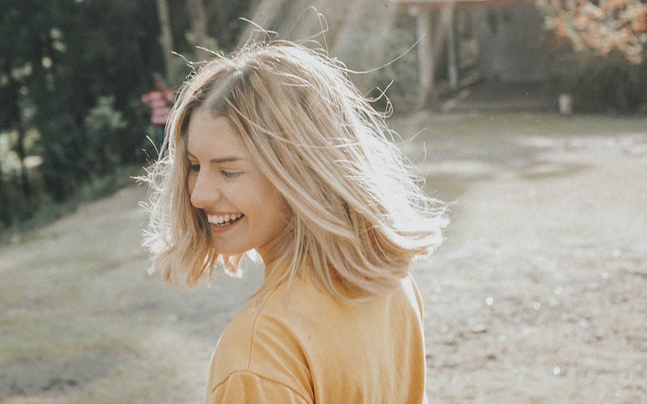 A woman in a yellow shirt is smiling while walking down a dirt road.