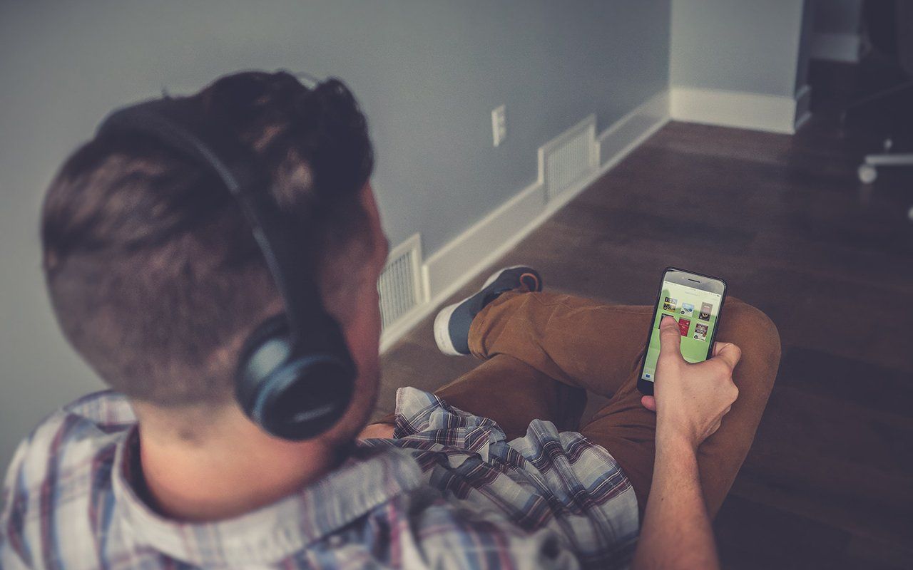 A man wearing headphones is sitting on the floor using a cell phone.