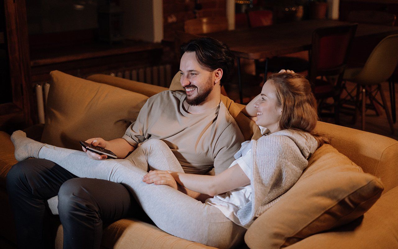 A man and a woman are sitting on a couch watching tv.