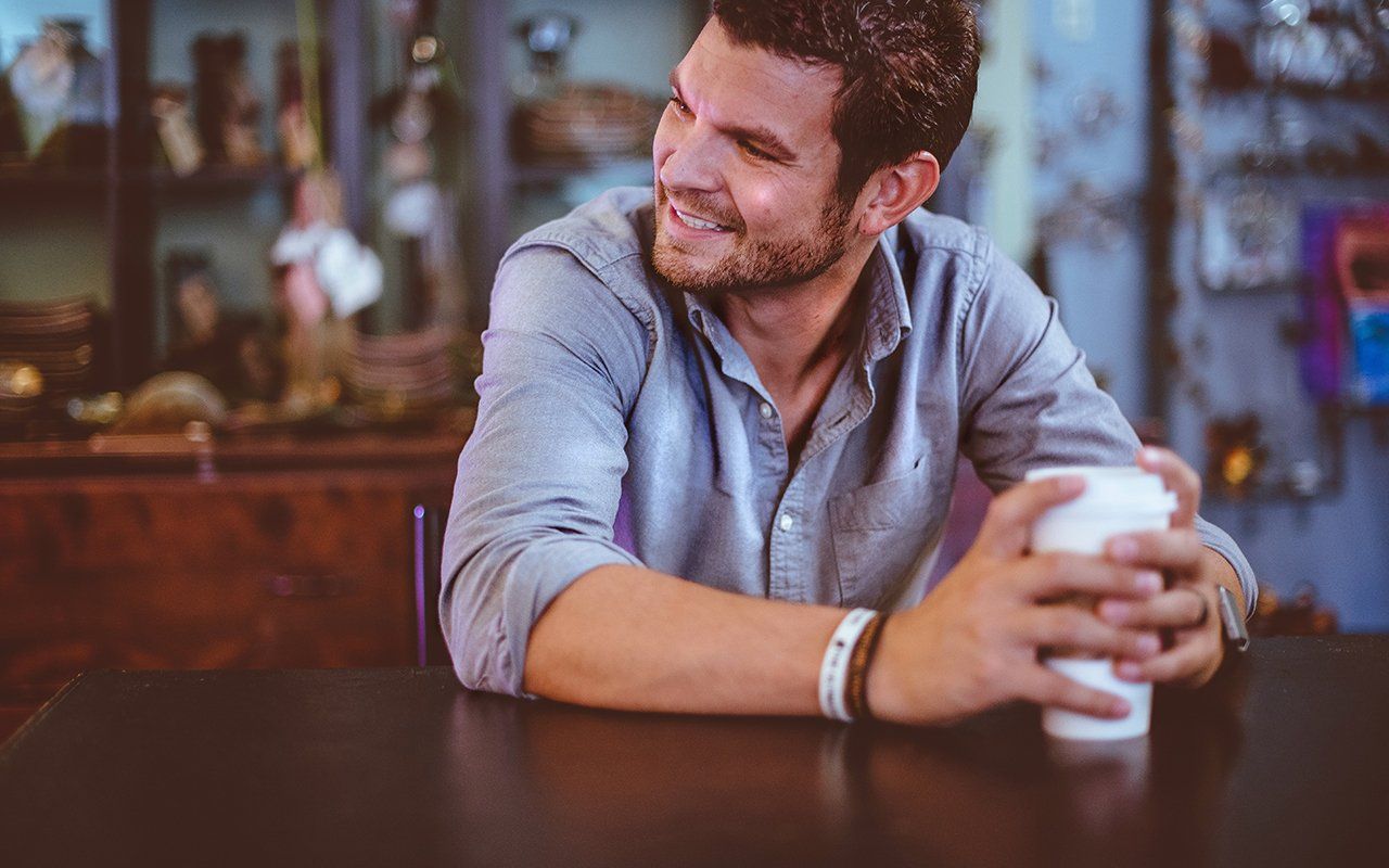 A man is sitting at a table holding a cup of coffee.