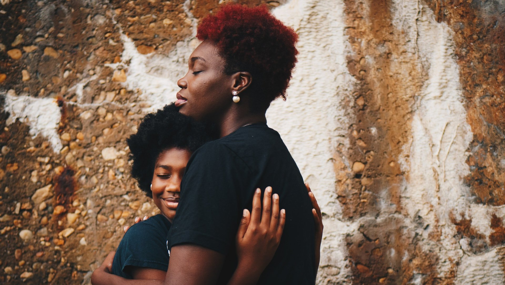 A woman and a child are hugging each other in front of a brick wall.