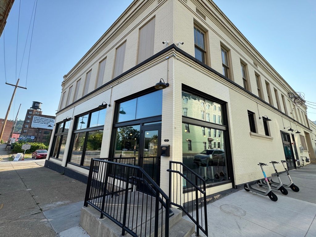 Corner street-level storefront with large windows, black railing, and scooters on the sidewalk under a blue sky