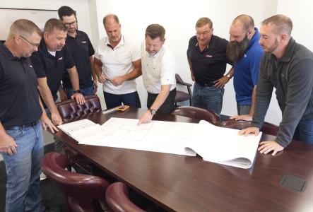 Team gathered around a conference table reviewing large blueprints in a meeting room.
