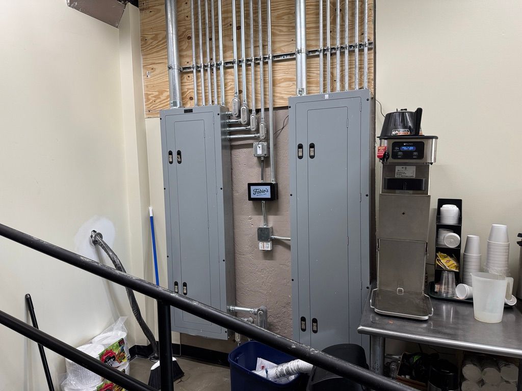 Electrical utility room with gray breaker panels, exposed wiring, and a stainless-steel counter with supplies