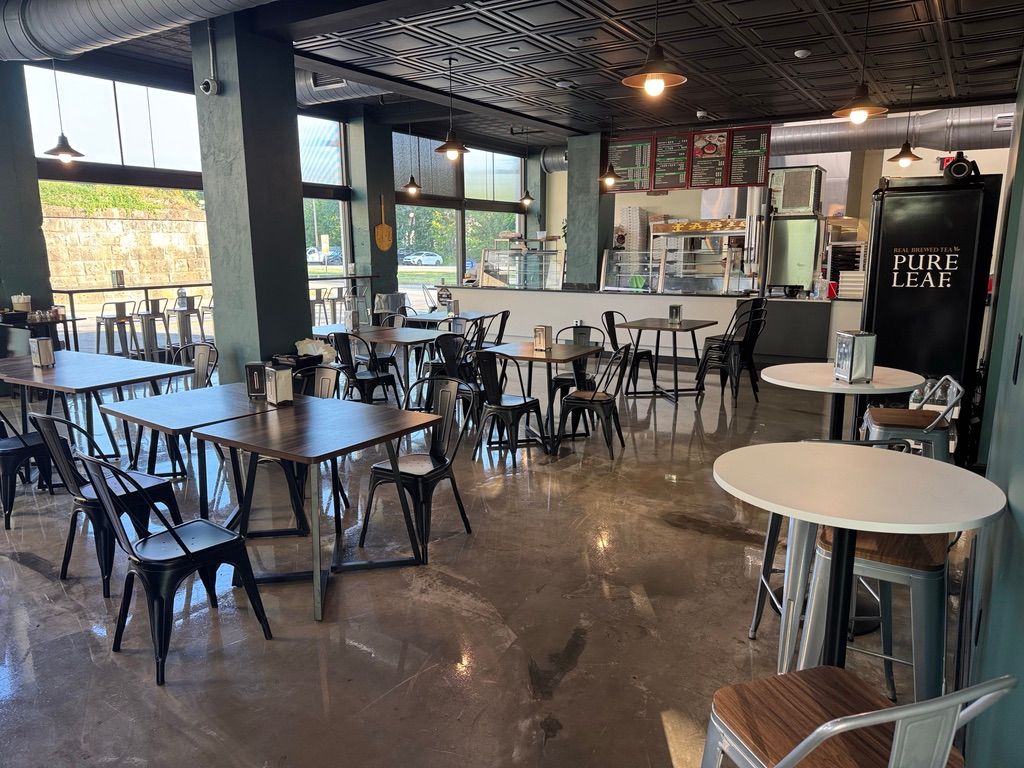 Empty café with tables and chairs, polished floor, and a decorative ceiling near large windows.