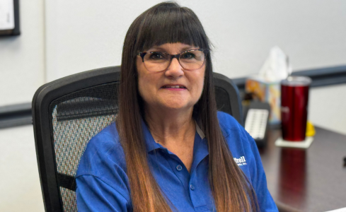 Smiling woman in glasses and blue shirt seated at an office desk