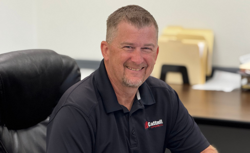 Smiling man in a black polo shirt seated at an office desk in a modern workspace
