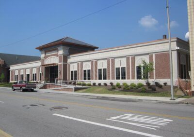 Large brick building with white trim and arched windows along a street under a clear blue sky