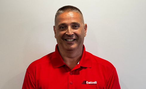 Smiling man in a red polo shirt standing against a plain light background.